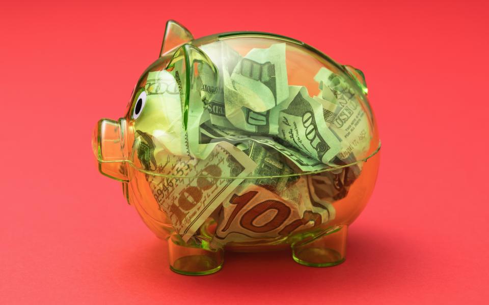 Clear piggy bank filled with dollars on a red background.