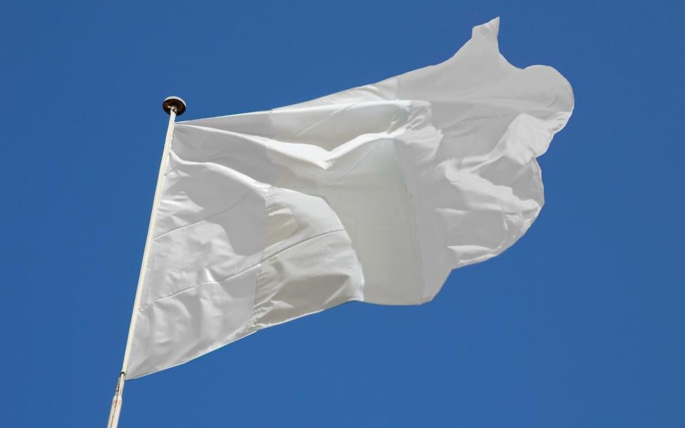A white flag billowing in front of a blue sky.
