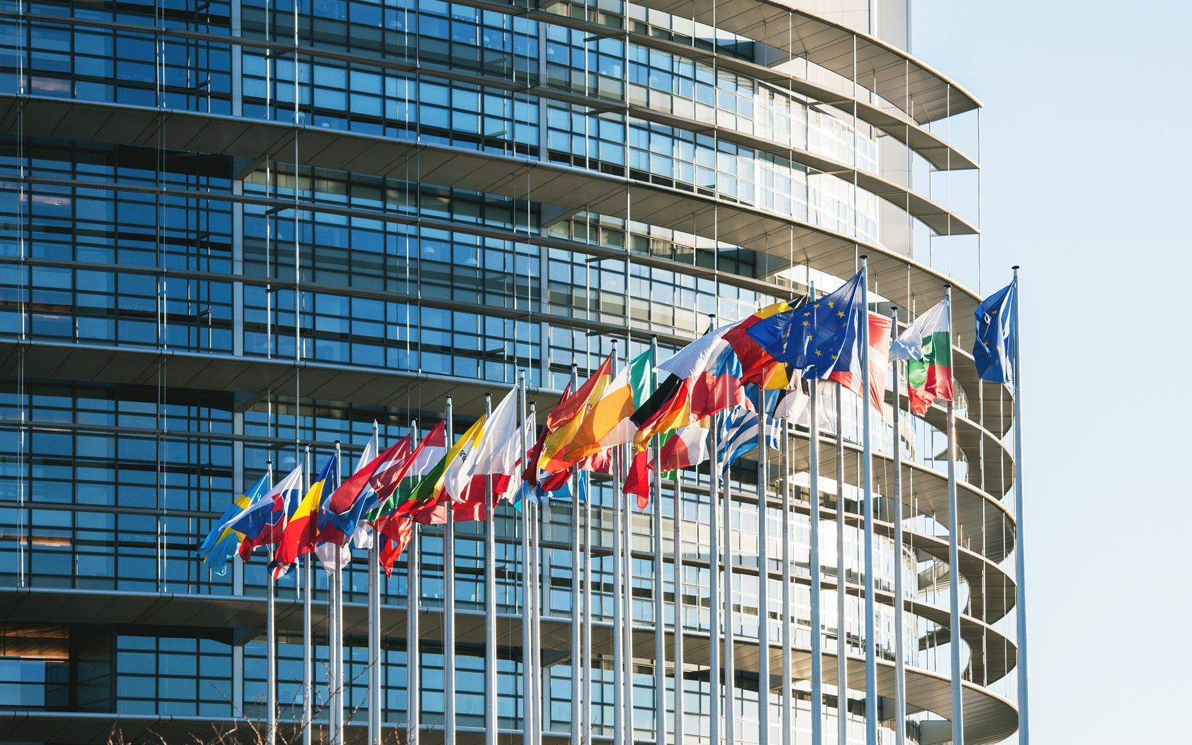 Array of international flags flying in front of glass + steel corporate building