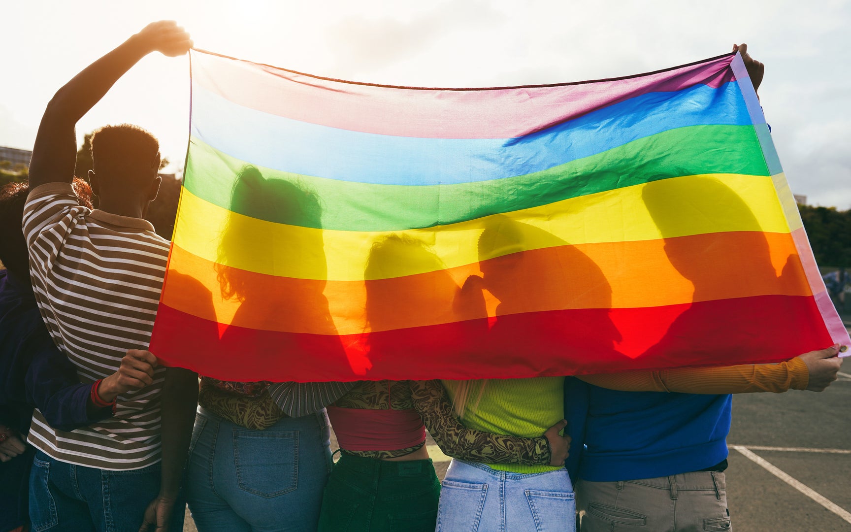 Young diverse people having fun holding LGBT rainbow flag outdoor.