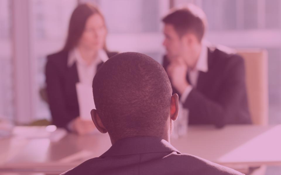 A black man being interviewed by two white colleagues with a pink overlay on the image.