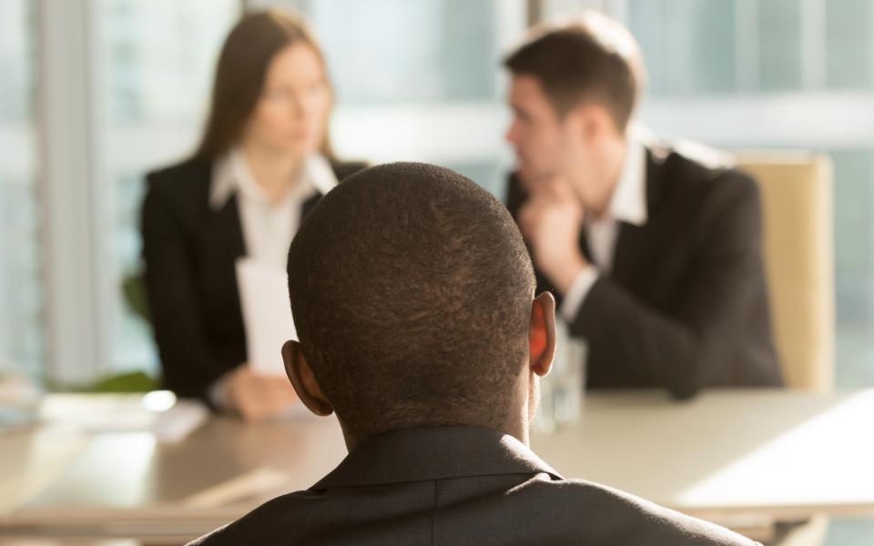 A black man being interviewed by two white colleagues. 