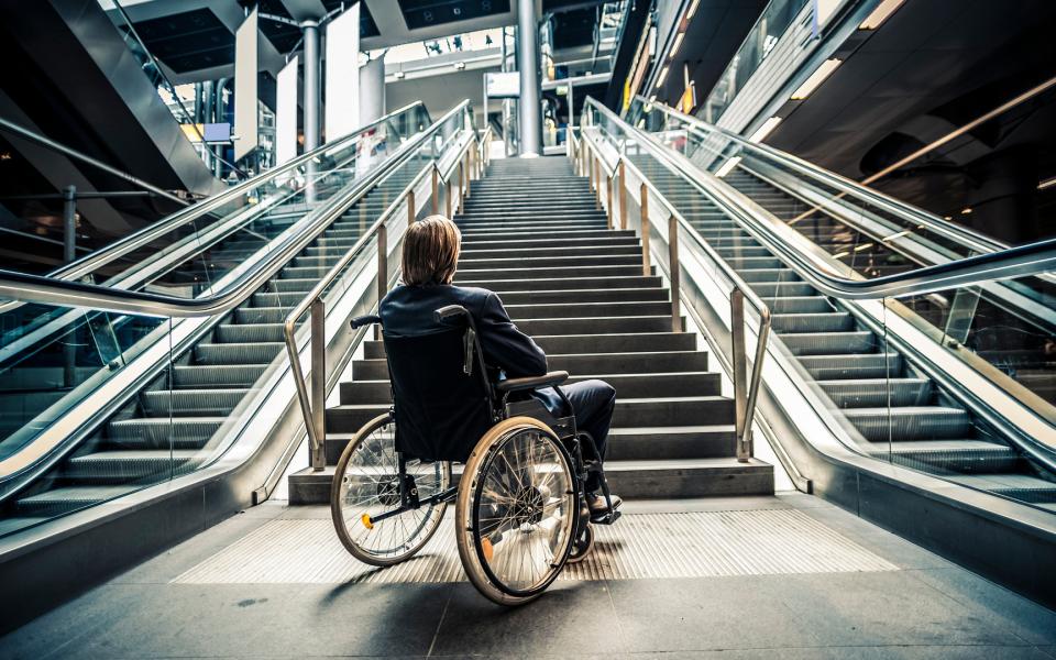 Businessman in a wheelchair facing stairs and escalators.