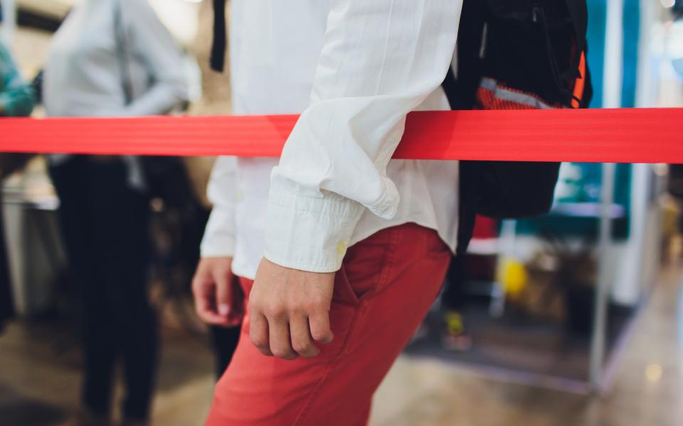 Blurred picture of long passenger queue stuck behind red ropes at airport.