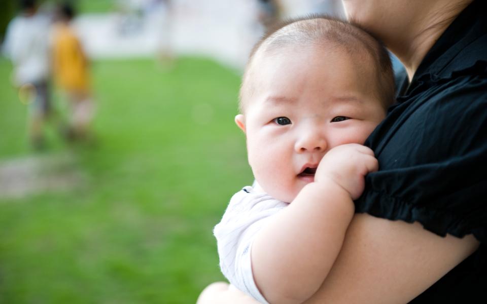 Close-up of an Asian baby boy being held in his mother's arms.