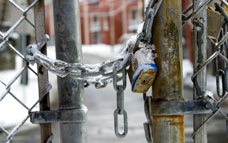 Close-up of a frozen padlock and chain locking a chainlink fence.