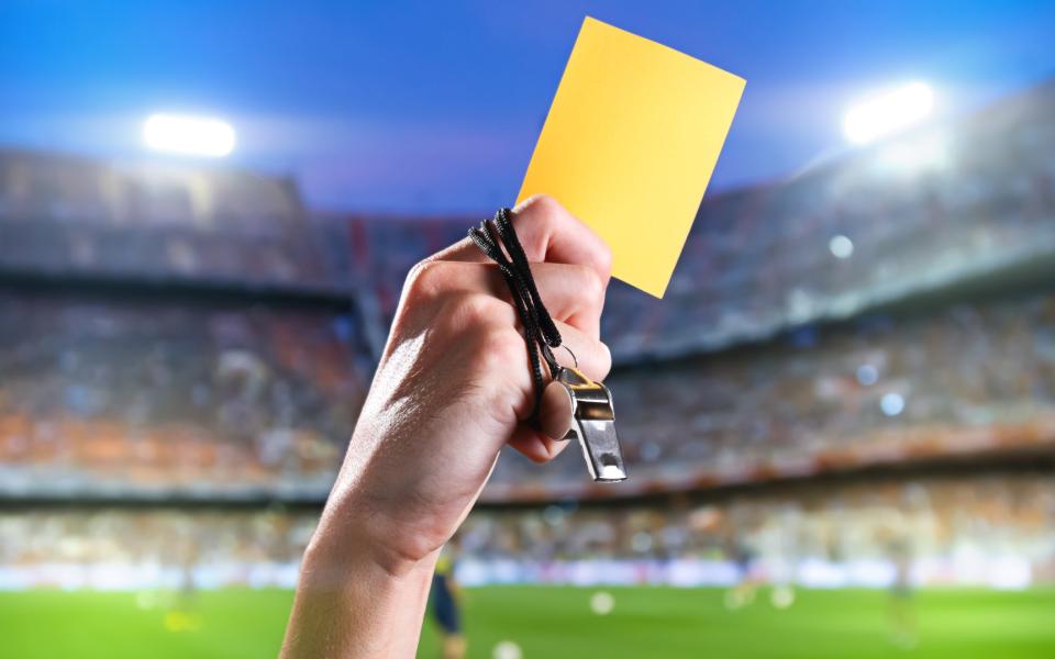 Hand of referee with yellow card and whistle in the soccer stadium.