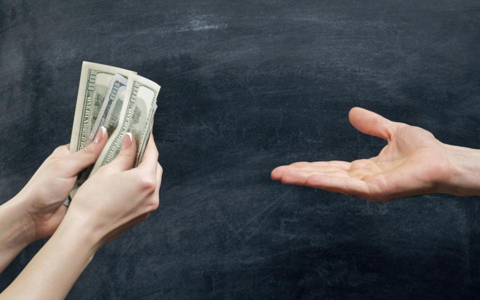 Close-up of two hands. One hand holding dollar bills and the other hand is open/outstreched asking for money.