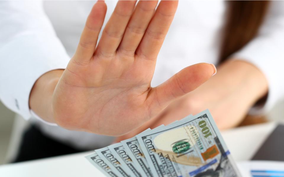 Close-up of a man holding up his hand to refuse money being handed to him.