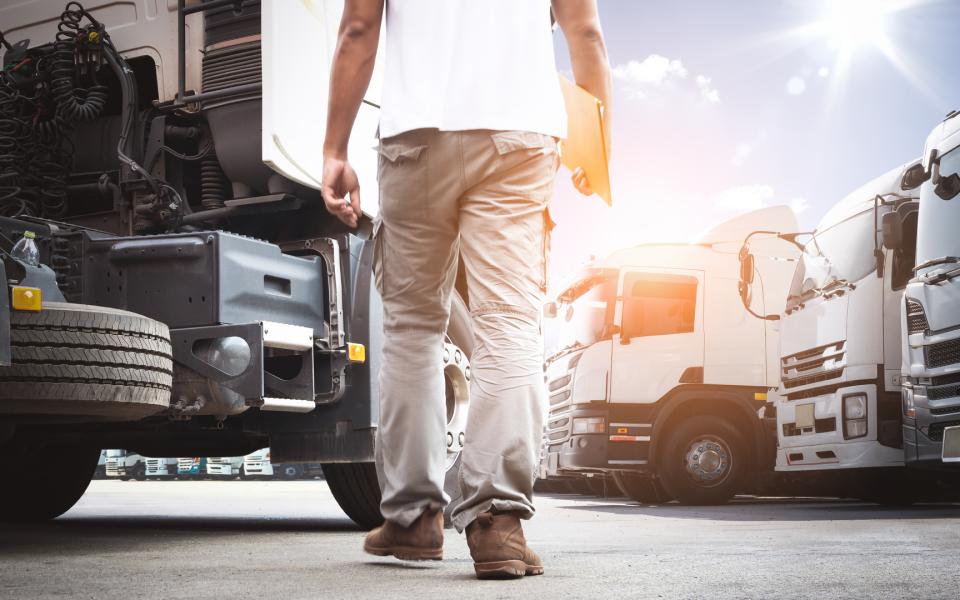 Close-up of the legs of a truck driver holding a clipboard walking among a fleet of big rigs.